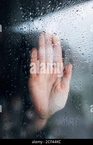 Unverkennbare verzweifelte Person, die am Fenster steht und nasses Dampf berührt Glas während der Verweilzeit in Selbstisolation zu Hause während Coronavirus Pandemie Stockfoto