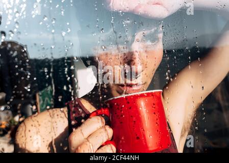 Nachdenkliche Frau trinkt Kaffee in der Nähe des Fensters Stockfoto