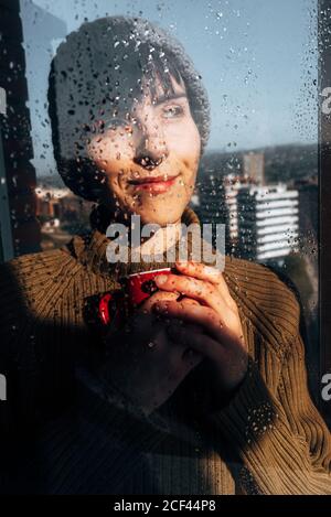Glückliche Frau, die Kaffee am Fenster trinkt Stockfoto