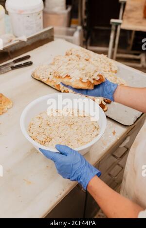 Von oben anonymen Konditor in Latexhandschuhe mit Schale Frische Mandelflocken und die Zubereitung von köstlichem Gebäck während der Arbeit in Bäckerei Stockfoto