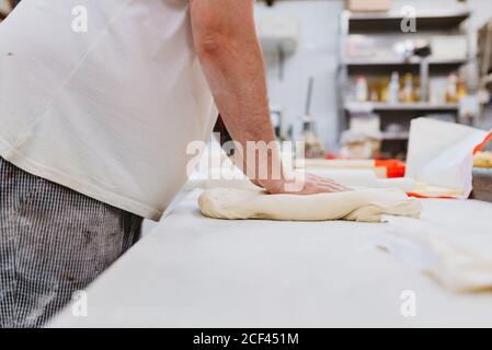 Seitenansicht der Ernte übergewichtigen Mann in Uniform Kneten weich Teig auf dem Tisch während der Arbeit in der Backküche Stockfoto