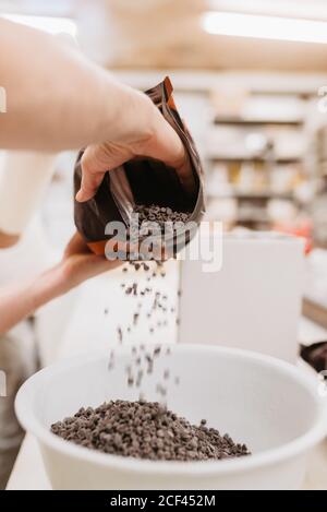 Nicht erkennbarer Arbeiter verschüttet Schokolade in Schüssel vor dem Schmelzen während Arbeiten in der Bäckerei Stockfoto