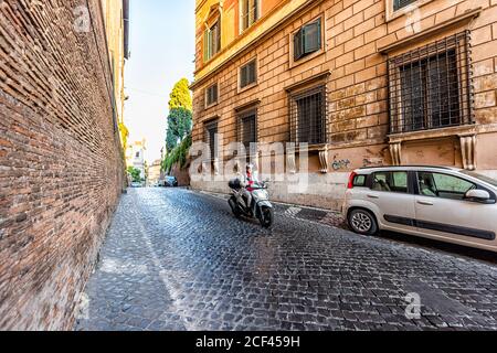 Rom, Italien - 5. September 2018: Italienische Kopfsteinpflasterstraße draußen in der historischen Stadt am Morgen und Frau Motorrad am Morgen Stockfoto