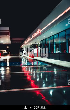 Verlassene alte Tankstelle mit Cafe und Parkplätzen Nacht mit Straßenlaternen, die sich in nassem Asphalt spiegeln Stockfoto