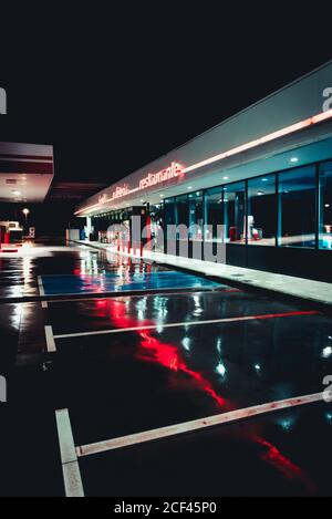 Verlassene alte Tankstelle mit Cafe und Parkplätzen Nacht mit Straßenlaternen, die sich in nassem Asphalt spiegeln Stockfoto