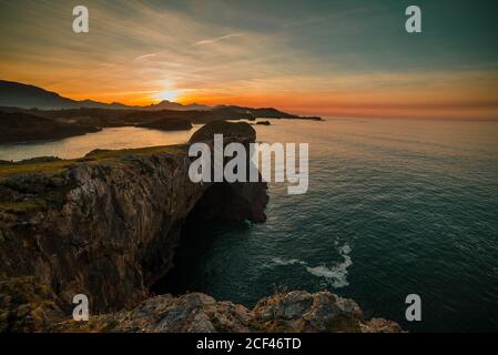 Panoramablick auf riesige Felsklippen über gewelltes Wasser gegen Sonnenuntergang Himmel, Asturien, Spanien Stockfoto