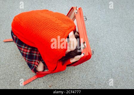 Von oben Frau in roten Pullover mit Spaß versuchen, in roten Koffer auf der Straße zu verstecken Stockfoto