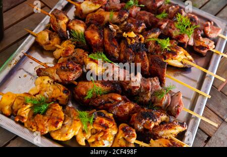 Nahaufnahme von appetitlich gegrillten Hähnchen und Schweinespieße garniert mit Frisches Grün auf Metalltablett serviert Stockfoto