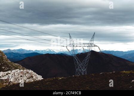 Hoher Strommast mit Hochspannungskabeln im Hochland gegen Schneebedeckte Bergrücken am Horizont unter grau bewölktem Himmel in Spanien Stockfoto