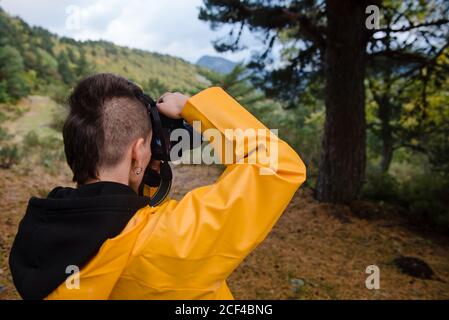 Rückansicht der jungen Person mit stilvollen Frisur Aufnahme Foto Von Baum im Bergtal in grauen Tag Stockfoto