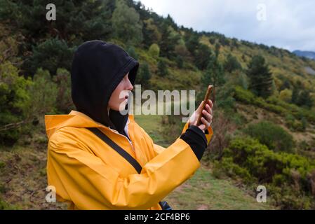 Frau im Hoodie und gelben Regenmantel Browsing Smartphone Stockfoto