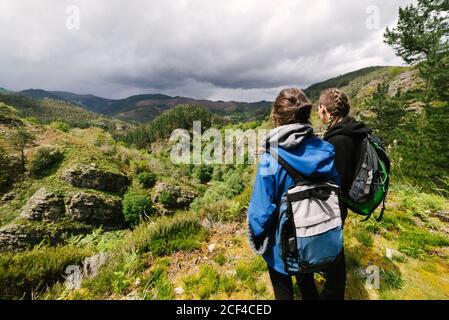 Rückansicht von nicht erkennbaren Wanderinnen in Oberbekleidung auf stehen Rocky Hill und bewundern erstaunliche Aussicht auf Hochland Landschaft während Sonniger Tag Stockfoto