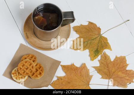 Tasse Tee und Waffeln. In der Nähe auf dem Tisch sind getrocknete Ahornblätter. Stillleben im Herbst. Stockfoto