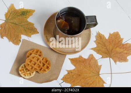 Tasse Tee und Waffeln. In der Nähe auf dem Tisch sind getrocknete Ahornblätter. Stillleben im Herbst. Stockfoto