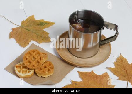 Tasse Tee und Waffeln. In der Nähe auf dem Tisch sind getrocknete Ahornblätter. Stillleben im Herbst. Stockfoto