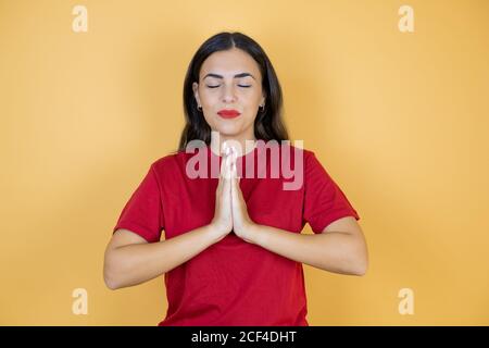 Junge schöne Frau trägt lässige rote T-Shirt mit geschlossenen Augen beten. Stockfoto