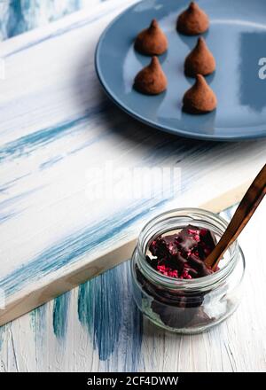 Von oben Glas mit leckeren Stücken von Schokolade mit Marmelade und hausgemachte Schokoladentrüffel auf dem Teller auf dem Holztisch Stockfoto