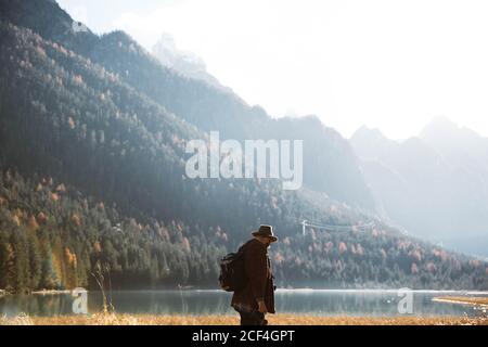 Rückansicht von anonymen Mann Reisenden in lässiger Kleidung mit Rucksacktouristen stehen und erfreuen in Aussicht auf türkisfarbenen See mit Neblige Dolomiten Berge im Hintergrund bei Italien Stockfoto