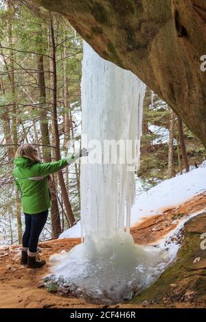 Frau inspiziert gefrorene Eissäulen in der Saltpeter Cave, Teil des Hocking Hills State Park Systems von Parks im südlichen Ohio, USA. Stockfoto