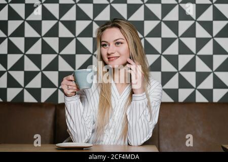 Frau mit Tasse frischen Kaffee lächelnd und wegschauen Beim Sitzen am Tisch im gemütlichen Restaurant Stockfoto