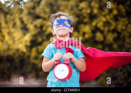 Superheld Kind Junge mit Wecker vor grünem Hintergrund im Freien. Kindheit, Erfolg und Machtkonzept Stockfoto