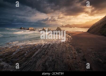 Landschaftlich schöner Blick auf den leeren Strand mit Steinen und Wellen Sonnenuntergang Hintergrund mit Regenwolken Stockfoto