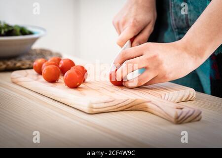 Anonyme Frau schneidet Tomaten, während sie in der Küche gesunden Salat kocht Stockfoto