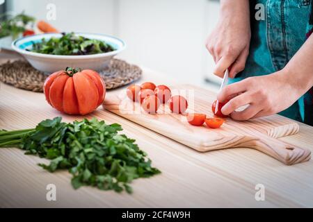 Anonyme Frau schneidet Tomaten, während sie in der Küche gesunden Salat kocht Stockfoto