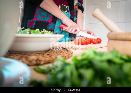 Anonyme Frau schneidet Tomaten, während sie in der Küche gesunden Salat kocht Stockfoto