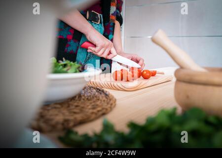 Anonyme Frau schneidet Tomaten, während sie in der Küche gesunden Salat kocht Stockfoto