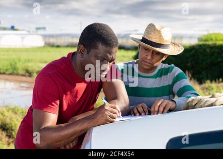 Portrait afrikanischer und hispanischer Gärtner, die draußen Papiere unterschreiben Stockfoto