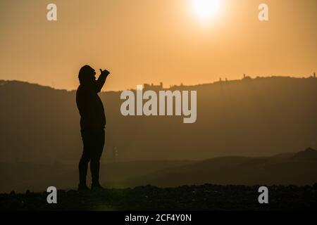 Silhouette des Touristen steht auf dem Feld in hellen Rücken beleuchtet von Sonnenuntergang Himmel, Italien Stockfoto