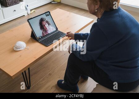 Von oben Seitenansicht des Ernteguts ältere weibliche sitzen an Tabelle und Online-Gespräch über Laptop mit Tochter, während Aufenthalt zu Hause während der Coronavirus-Pandemie Stockfoto