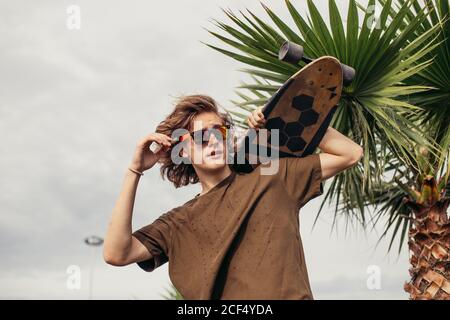 Stattliche skateboarder Repowering Sonnenbrille hält Longboard auf die Schulter auf Stadt Straße oder tropic Hintergrund Stockfoto