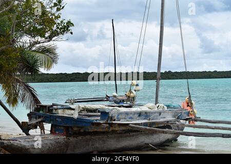 Eine Nahaufnahme eines kleinen lokalen Bootes, das an einem tropischen Strand auf Isle of Pines, Neukaledonien gebunden ist. Das Holzboot ist im Stil eines Katamarans. Stockfoto