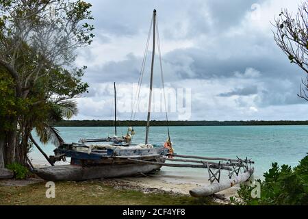 Ein lokales Boot, das entlang des Ufers eines tropischen Strandes auf Isle of Pines, Neukaledonien, gebunden ist. Das Boot ist aus Holz und hat Angelzubehör an Bord. Stockfoto