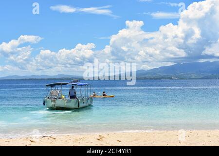 Zwei Kajakfahrer fahren an einem kleinen Boot vorbei in den Gewässern um South Sea Island, Teil der Mamanuca Inseln in Fidschi. Goldener Sand und blaues ruhiges Meer. Stockfoto