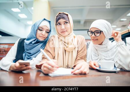 Drei muslimische Frauen im Hijab sitzen am Tisch und schreiben Stockfoto