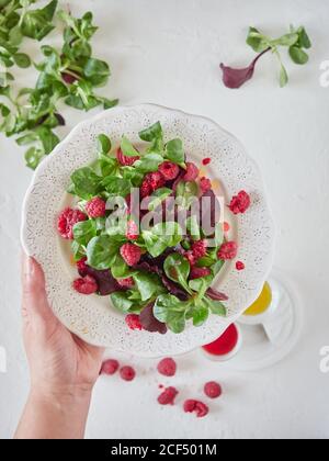 Von oben Ernte kochen halten Zierplatte mit leckeren frischen Salat mit reifen Himbeeren und frischem Spinat Stockfoto