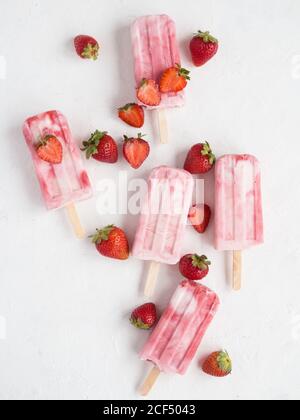 Von oben köstliche erfrischende rosa Freeze Pops und Bündel Frische Erdbeeren auf weißem Hintergrund Stockfoto