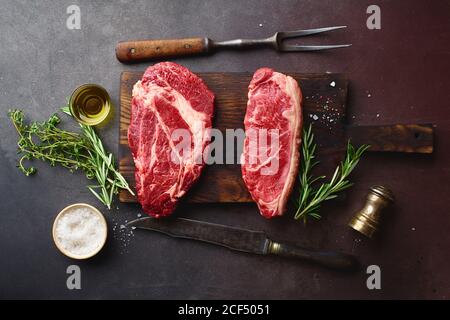 Draufsicht auf rohe schwarze angus Prime Beef Steaks auf Holzschneidebrett: Chuck Roll und Striploin. Stockfoto
