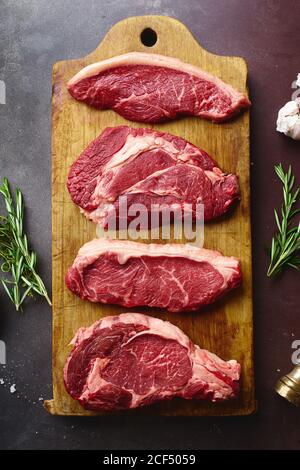 Draufsicht auf rohe schwarze angus Prime Beef Steaks auf Holzschneidebrett: Rib Eye, Chuck Roll, Striploin und Picanha. Stockfoto