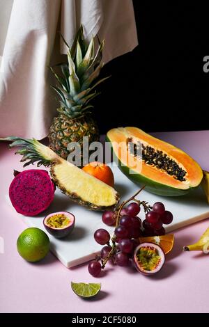 Stillleben mit tropischen Früchten: Geschnittene Papaya, Ananas, Pitaya und Trauben auf Marmor Schneidebrett Stockfoto
