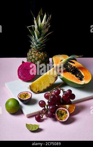 Stillleben mit tropischen Früchten: Geschnittene Papaya, Ananas, Pitaya und Trauben auf Marmor Schneidebrett Stockfoto