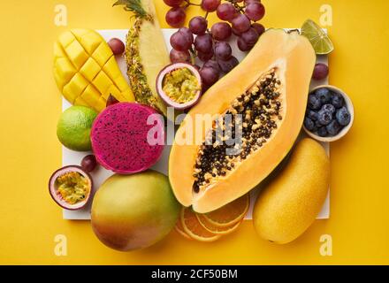 Draufsicht auf flaches Lay mit tropischen Früchten auf einem Tablett: Papaya, Mango, Drachenfrucht und Ananas auf gelbem Hintergrund. Sommergenuss Stockfoto