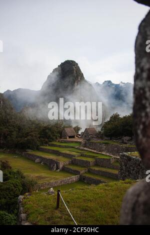 Herrliche Aussicht auf grüne felsige Tal mit Steinzäunen und Kleine Steinhäuser in der Nähe von Gipfel von nebligen Wolken bedeckt In Peru Stockfoto