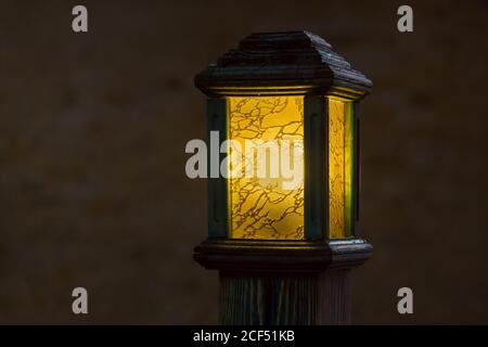 Hölzerne Straßenlampe mit gelbem Glasdiffusor, alter Lichtmast glüht warm am Abend Nahaufnahme mit Kopierraum, niemand. Stockfoto