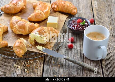 Frühstück mit frisch gebackenen Croissants auf einem Kühlregal, serviert mit Butter, Marmelade und einer Tasse Kaffee-Creme Stockfoto