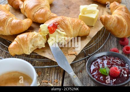 Frühstück mit frisch gebackenen Croissants auf einem Kühlregal, serviert mit Butter, Marmelade und einer Tasse Kaffee-Creme Stockfoto