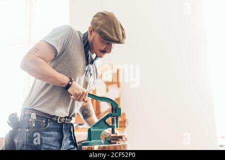 kaukasische Leder Handwerk Schnurrbart Mann trägt Tasse arbeiten als Handwerker In seiner Werkstatt Stockfoto